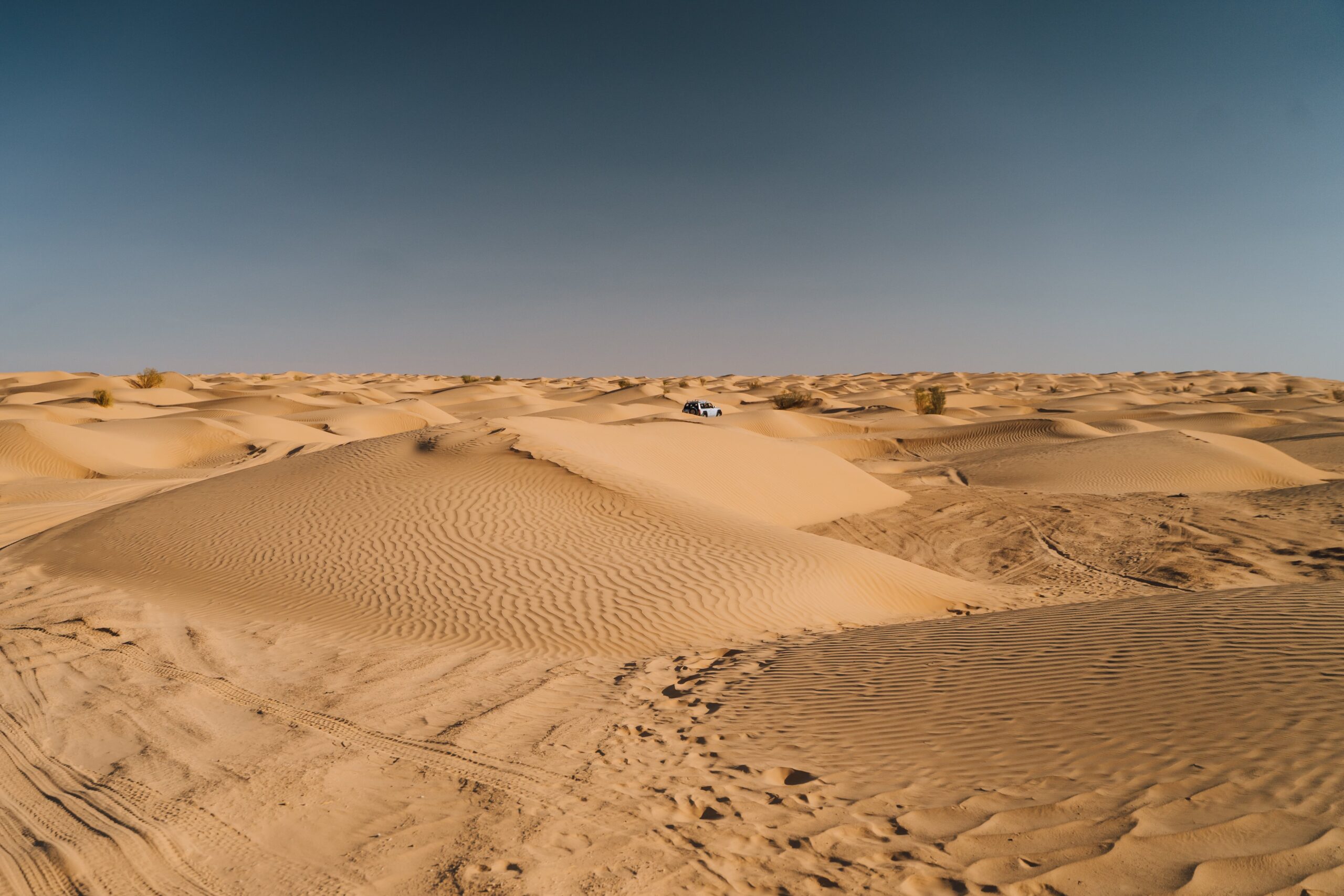 4x4 vehicle driving through the vast sand dunes of the Sahara Desert, Tunisia, under a clear sky.