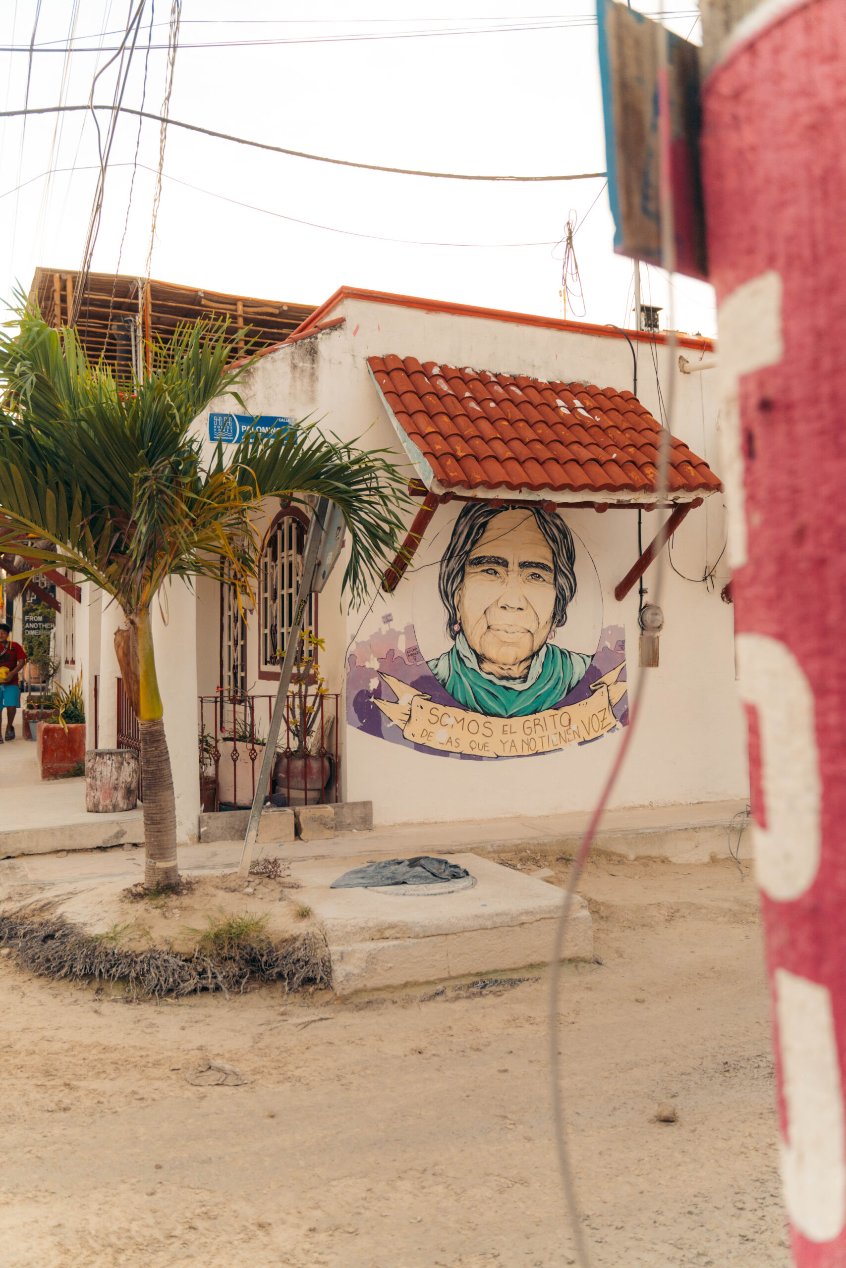 Mural of an old woman with the phrase 'Somos el grito de las que ya no tienen voz' in Holbox town center.